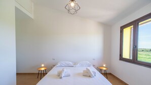 Habitación de hotel minimalista con una cama grande, dos mesitas de noche, una lámpara de diseño geométrico y un ventanal con vistas.