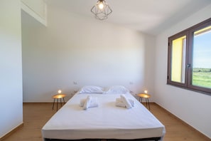Ein schlicht eingerichtetes Hotelzimmer mit einem großen Bett, zwei Nachttischen, einer geometrischen Leuchte und einem Fenster mit Aussicht.