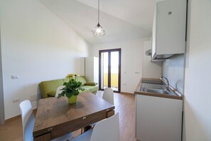 Eine moderne Küche mit integriertem Spülbecken, einer Essecke mit Holztisch und -stühlen, einem grünen Sofa und einem Blumentopf.