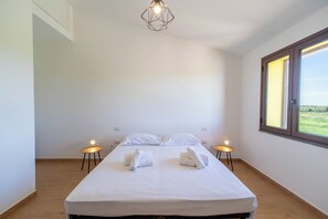 Ein schlicht eingerichtetes Hotelzimmer mit einem großen Bett, zwei Nachttischen, einer geometrischen Leuchte und einem Fenster mit Aussicht.