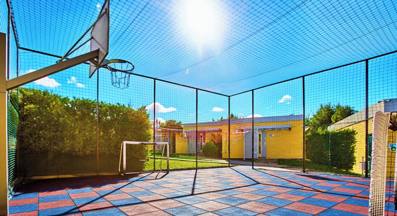 Un campo da basket all'aperto con canestro, rete e pavimento piastrellato.