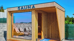 A sauna with a wooden exterior, a glass door, and a view of lounge chairs outside.