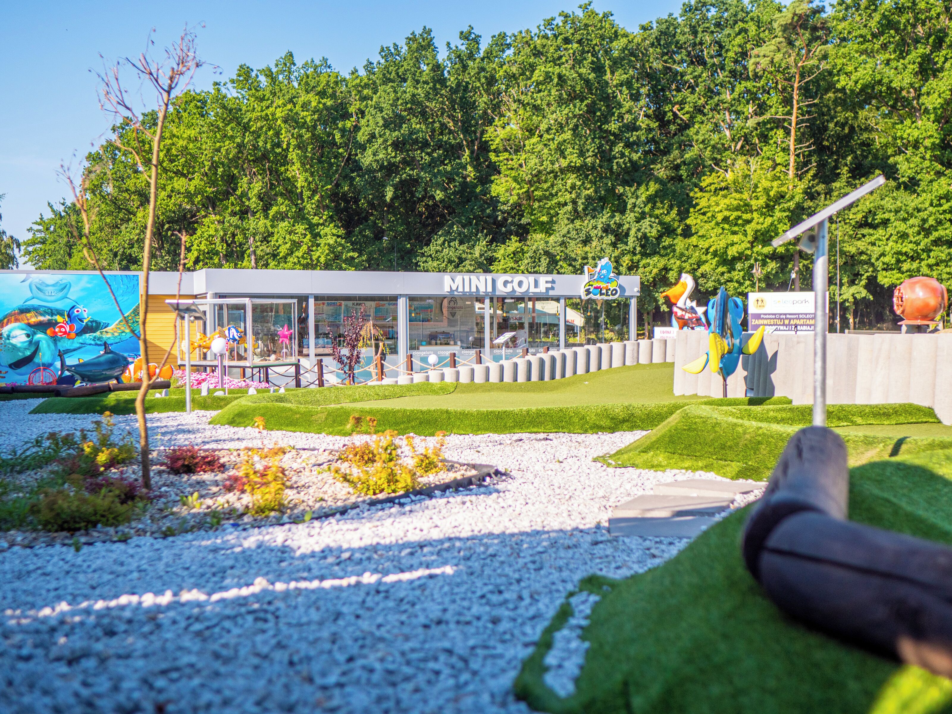 En minigolfbane med en tydelig sti, en bygning med teksten 'Mini Golf' og et muralmaleri af havdyr.