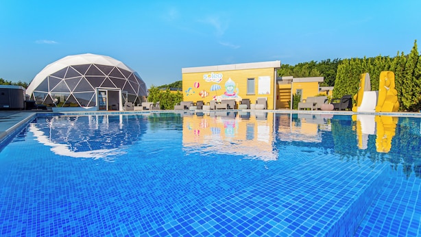 A swimming pool with a clear blue tile, a dome-shaped structure, and a building with a yellow facade.