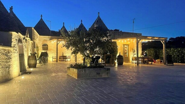 A stone building with multiple pointed roofs, a paved courtyard, and outdoor seating areas. - Apulian trullo with pool among vineyards (Martina Franca)