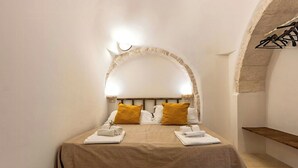 A bedroom with a bed, two pillows, a nightstand, and a wooden shelf. - Apulian trullo with pool among vineyards (Martina Franca)