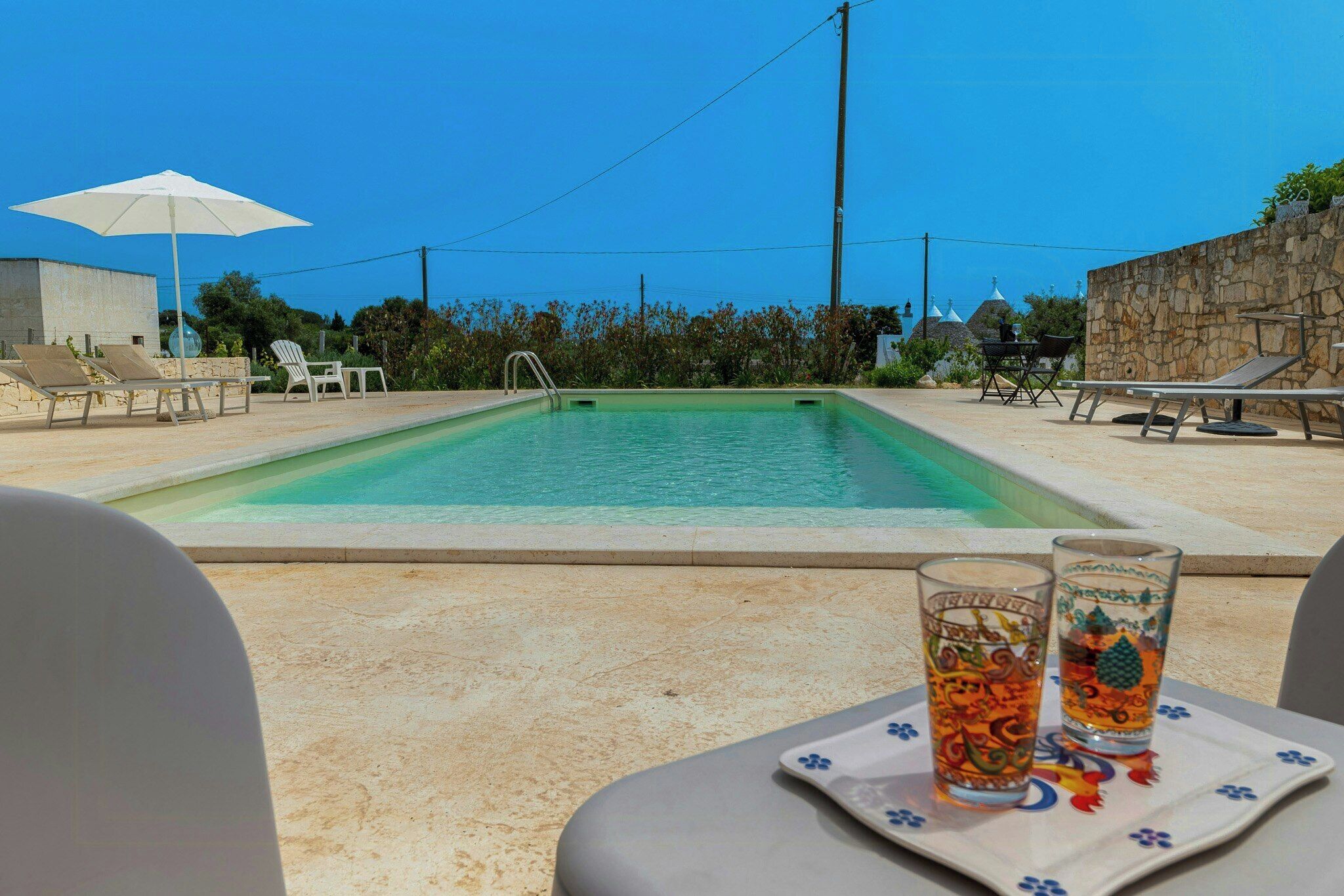 Una piscina con sillas de descanso y una mesa con dos vasos.
