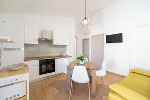 Eine moderne Küche mit weißen Schränken, einer Holzauskleidung, einem Esstisch mit Stühlen und einem gelben Sofa.