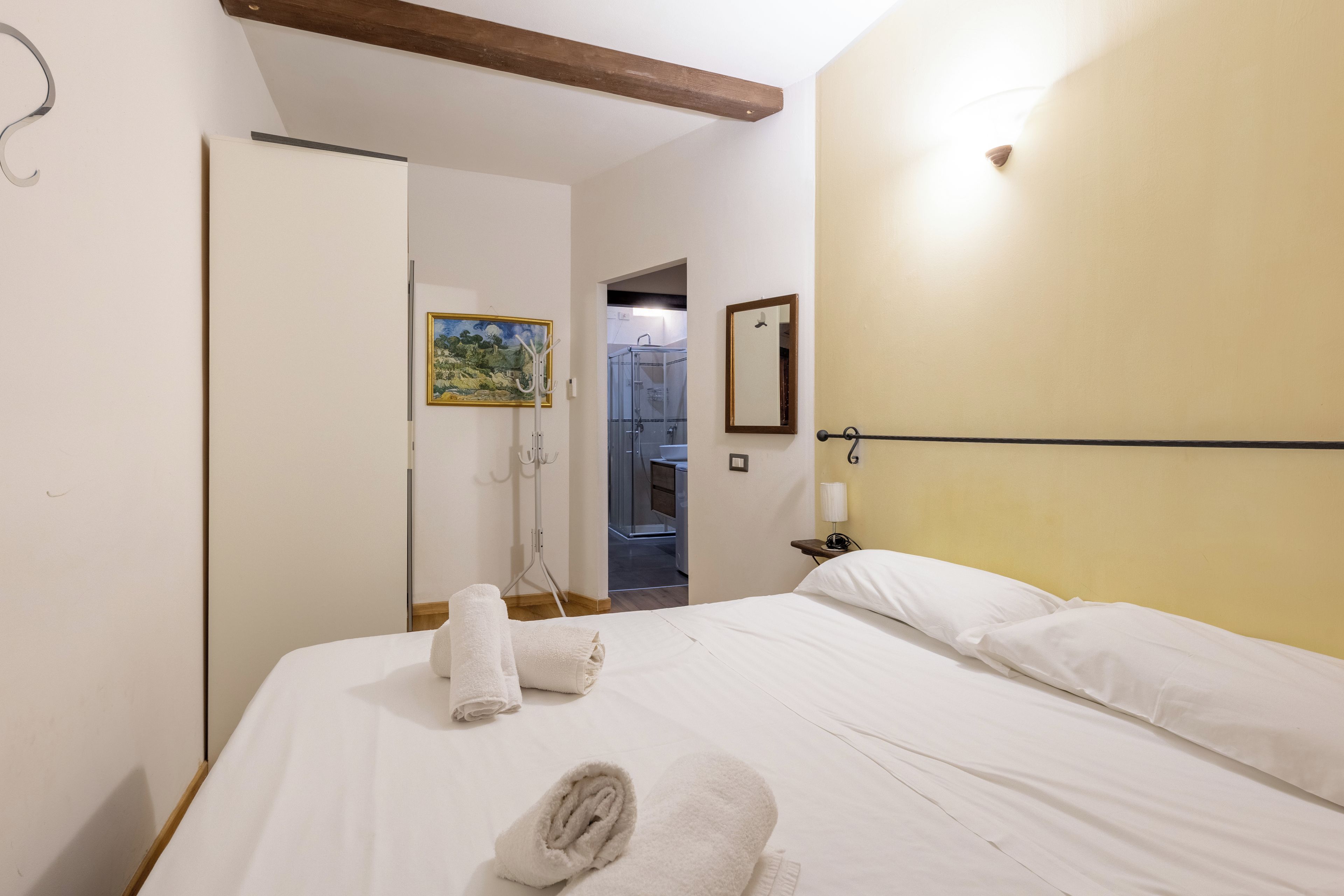 Une chambre d’hôtel avec un lit, une serviette, un tableau, un miroir et un espace douche.