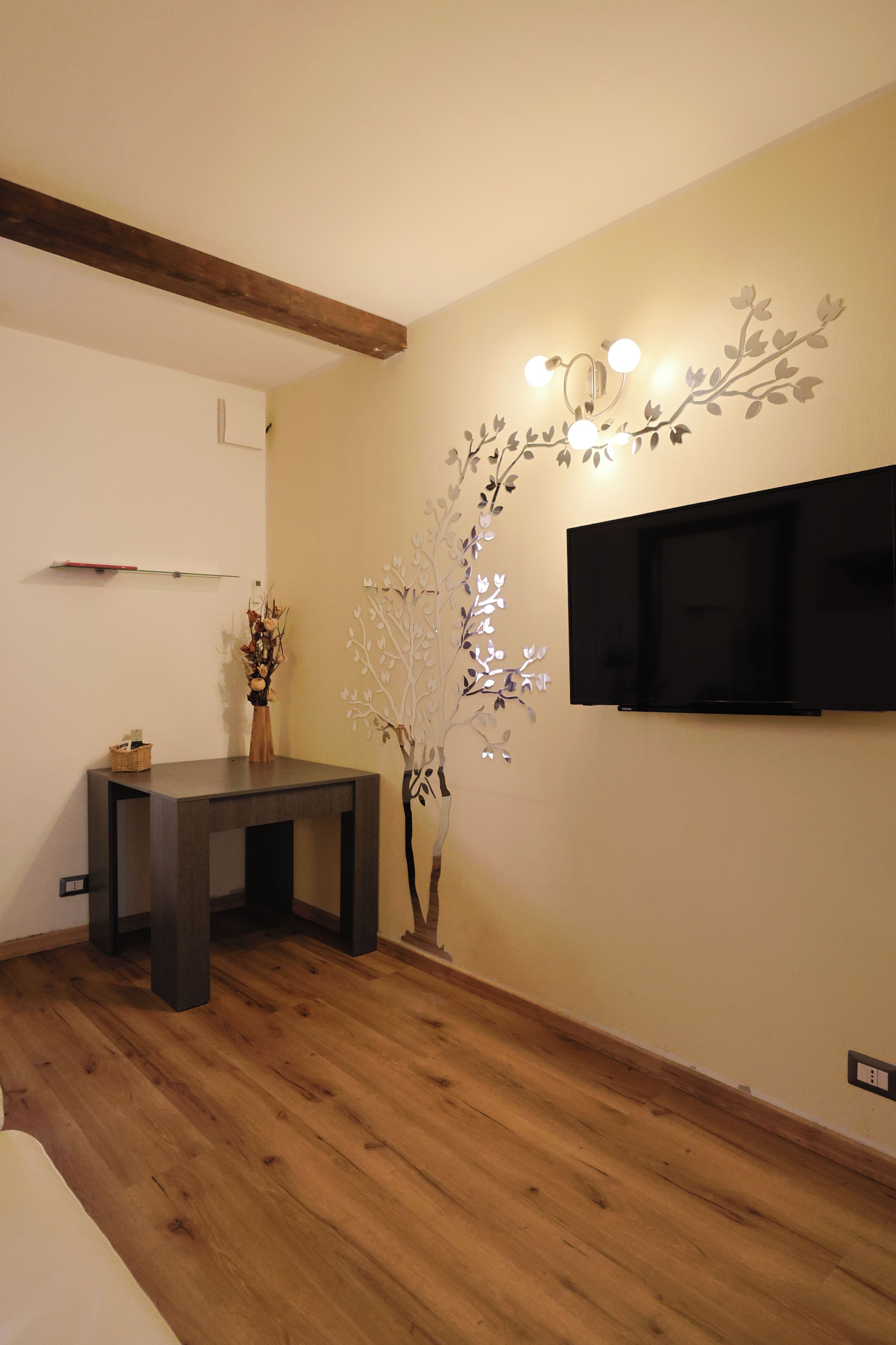 Una stanza con pavimento in legno, un tavolo scuro in legno, una TV a parete e un albero decorativo con luci.