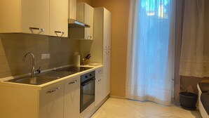 Een kleine keuken met een spoelbak, fornuis, oven en kastjes.