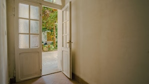 A hallway with a white door leading to an outdoor area with a tree and a bicycle. - Domus Dantis Piano Primo (Ravenna)
