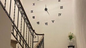 Een trap met gedetailleerd metalen hekwerk, een wandklok en een tafeltje met een plant.