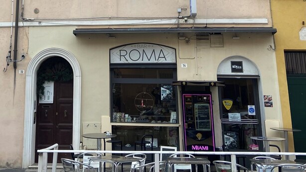 Een gebouw met meerdere ramen, een gevel waarop 'ROMA' staat, en terrasjes.