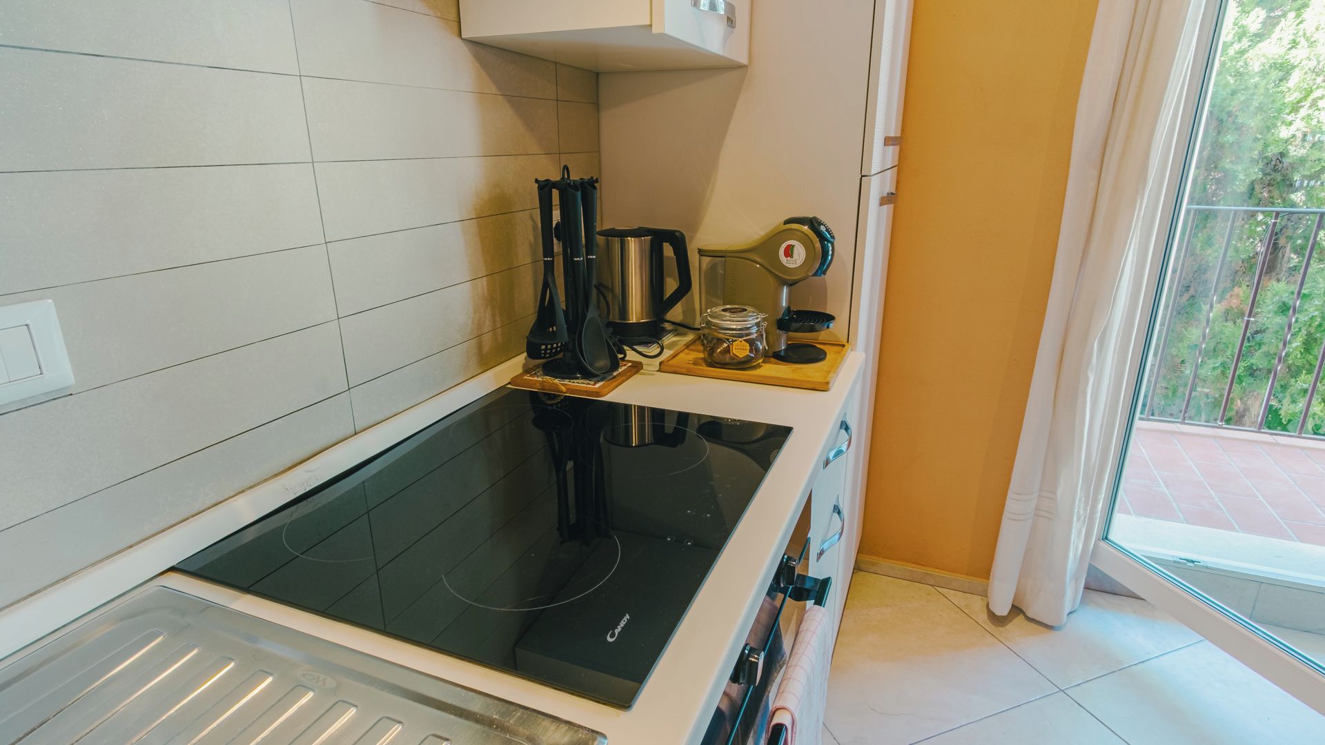 Een kleine keuken met een zwart inductiekookplaatje, een koffiezetapparaat en een waterkoker op het aanrecht.