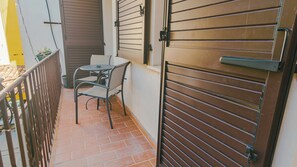Un balcon avec une table et des chaises, un portail métallique fermé et un sol carrelé.