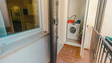 A laundry area with a washing machine, a red basket, and a green bucket.