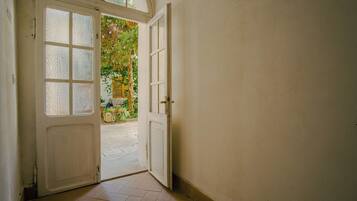 A hallway with a white door leading to an outdoor area with a tree and a bicycle.