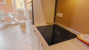 A kitchen with a black induction cooktop, white cabinets, and a glass dining table. - Domus Dantis Paradiso (Ravenna)