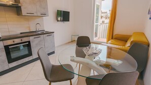 Een moderne keuken met een inbouwoven, een eethoek met een glazen tafel en stoelen, en een gele bank.