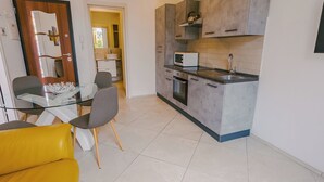 A modern kitchen with a microwave, oven, and sink. There is a dining area with a glass table and chairs. - Domus Dantis Vita Nova (Ravenna)