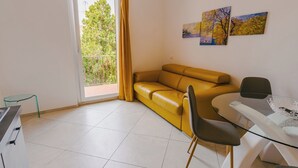A modern living room with a yellow sofa, a glass table, and a chair. There is a balcony with a view of trees and a building. - Domus Dantis Vita Nova (Ravenna)