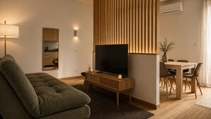 Una sala de estar moderna con sofá, televisión, pared de paneles de madera, comedor y cocina.