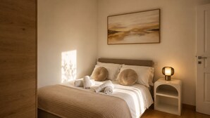 Un dormitorio con cama, almohadas, una mesita de noche con lámpara y un cuadro en la pared.