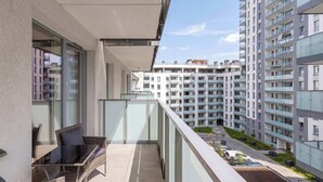 Un balcon agrémenté de meubles en osier, d’une table en verre et offrant une vue sur de grands immeubles d’habitation.