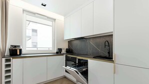 Une cuisine moderne avec des meubles blancs, un four encastré et une fenêtre au-dessus de l’évier.