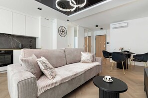 Ein modernes Wohnzimmer mit einer Couch, einem Esstisch mit Stühlen, einer Küchenzeile und einer Deckenleuchte.