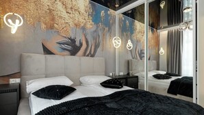 Une chambre moderne avec un grand lit, une table de chevet, un miroir et un mur orné d’une fresque à motifs.