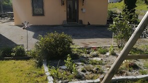 Um edifício com porta, janela com grade decorativa e área pavimentada com plantas e pedras.