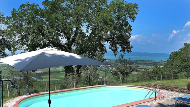 Une piscine dotée d’une plage en pierre, entourée d’arbres et offrant une vue sur le paysage.