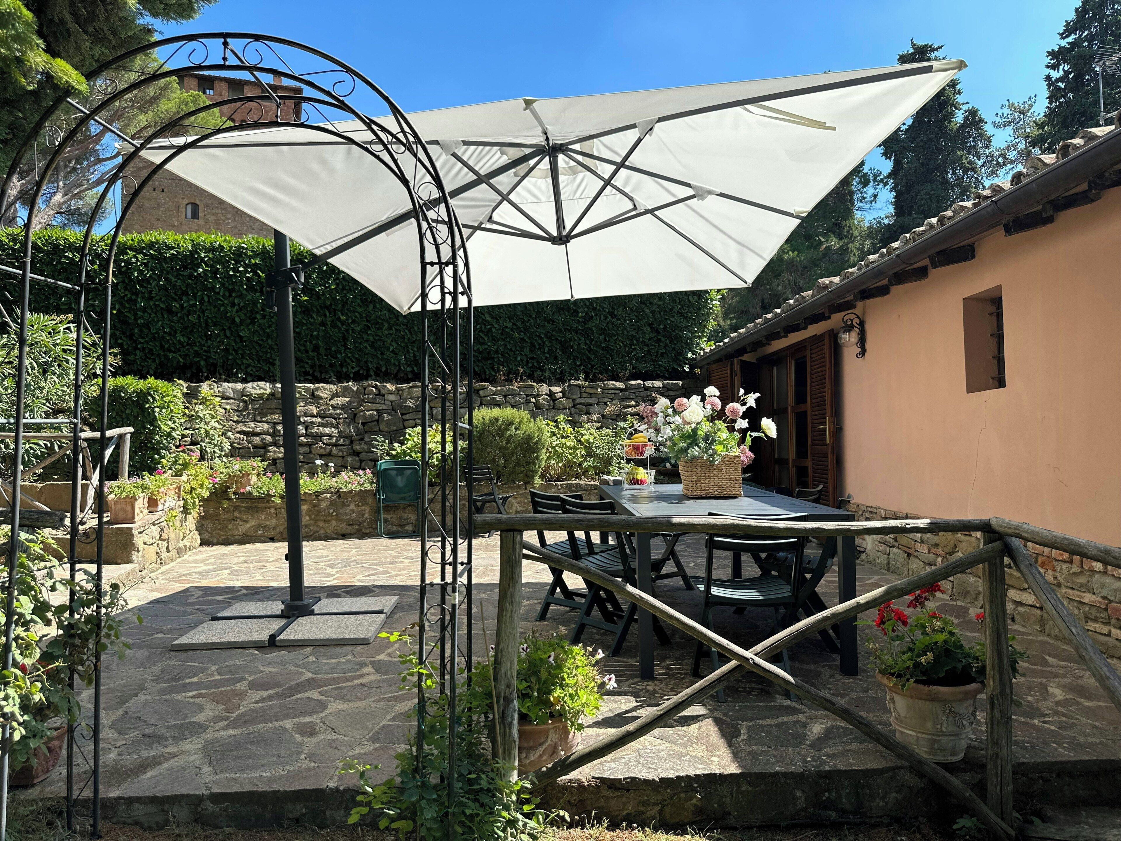Eine Terrasse im Freien mit Tisch, Stühlen, einem großen Sonnenschirm und Blumentöpfen.