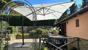 Une terrasse extérieure avec une table et des chaises, un grand parasol et des plantes en pot.