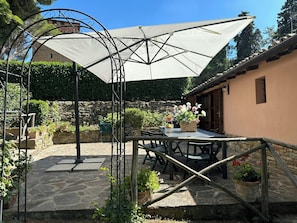 Eine Terrasse im Freien mit Tisch, Stühlen, einem großen Sonnenschirm und Blumentöpfen.