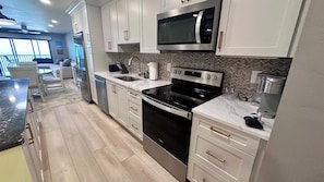 A modern kitchen with white cabinetry, a black oven, and a microwave. - Riviera Club 1103 - Direct Beach Access (Fort Myers Beach)