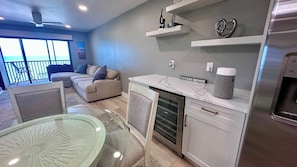 A modern kitchen with a built-in oven, a dining area with a glass table, and a living area with a sofa and a view of the ocean. - Riviera Club 1103 - Direct Beach Access (Fort Myers Beach)