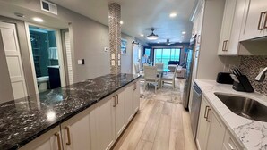 A modern kitchen with marble countertops, stainless steel appliances, and a view to the living area. - Riviera Club 1103 - Direct Beach Access (Fort Myers Beach)