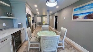 A modern kitchen with a built-in oven, a dining area with a glass table and white chairs, and a painting on the wall. - Riviera Club 1103 - Direct Beach Access (Fort Myers Beach)