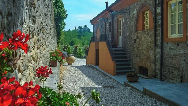 A courtyard with a stone wall, a building with a wooden staircase, and potted plants. - Violetta Apartment near Lucca (Segromigno in Monte)