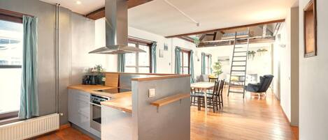 A modern kitchen with a central island, wooden flooring, and a loft bedroom with a ladder.