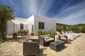 A white building with a patio area featuring wicker furniture, a table, and chairs. - 3-bedroom Villa in Sant Josep With Pool (Sant Josep de sa Talaia)
