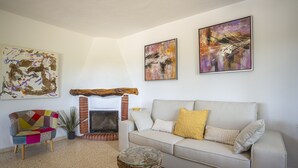 Ein Wohnzimmer mit einer Couch, einem bunten Sessel, einem Kamin und abstrakten Kunstwerken an den Wänden.