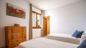 Ein Schlafzimmer mit zwei Betten, einem Holzschrank, einem Gemälde und einem Fenster mit Vorhängen.