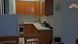 A compact kitchen with wooden cabinets, a built-in oven, a coffee maker, and a dining table with chairs.