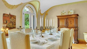Une salle à manger avec une table dressée pour six personnes, un lustre et une grande fenêtre.