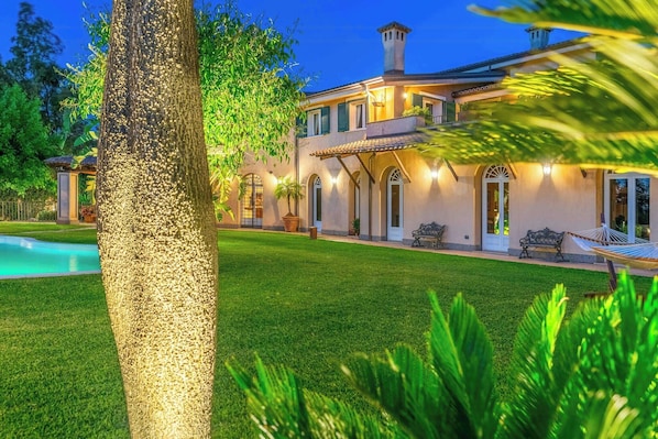 A large house with a swimming pool, surrounded by well-maintained lawns and trees.