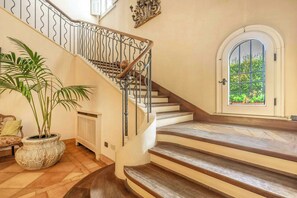 A staircase with a wrought iron railing, a potted plant, and a view through a window.